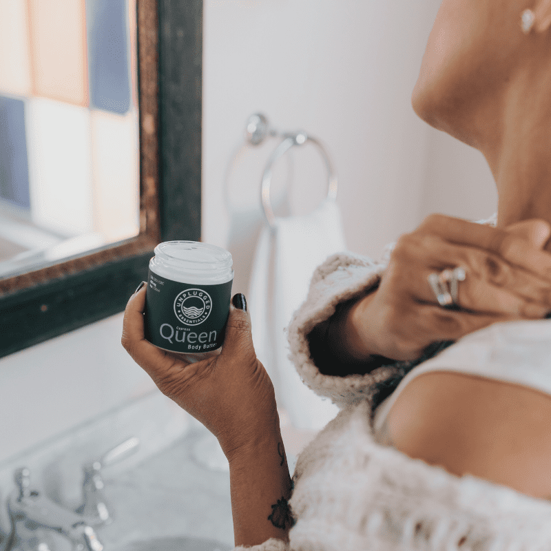 A woman applying the Queen Body Butter from Unplugged Essentials to her neck.